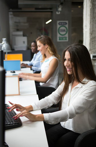 Group of businesswomen working in office. Selective focus on beautiful smiling women using computer.