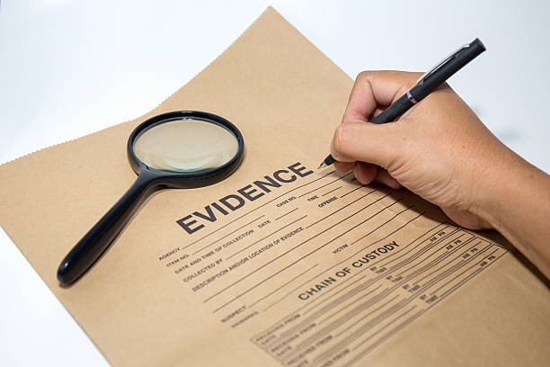 hand with pen writing on evidence paper with magnifying glass stock photo