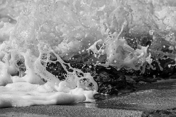 Frothy Ocean Waves in Black and White Waves crashing on the beach creating frothy foam. black and white beach stock pictures, royalty-free photos & images