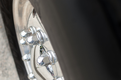 A close-up of a semi-truck's wheel and tire. Shiny chrome lug nuts are in focus, while the tire rubber, provides ample room for copy.