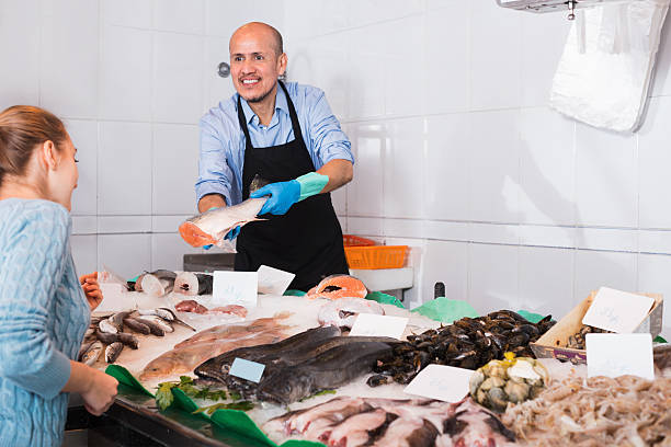istock Mature seller helping female customer to choose fish 528051846