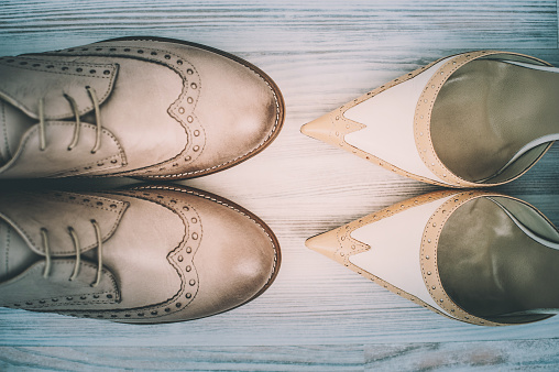 Close-up of two pair of couple's wedding shoes on hardwood floor, toned image.