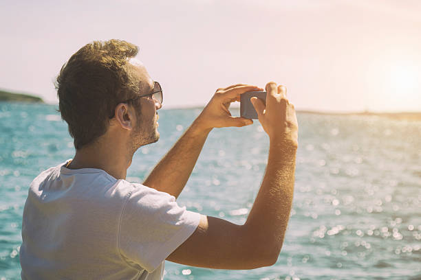 istock Hipster man taking photos with camera at the beach. 528059390