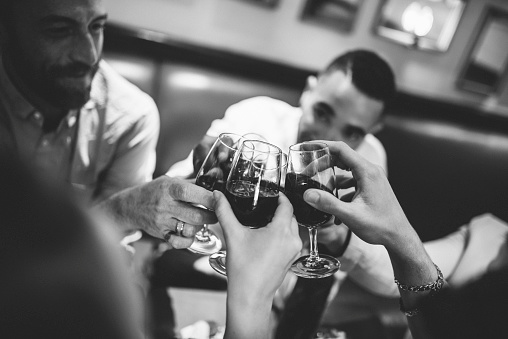 Multi ethnic group of friends toasting with red wine in a bar. They are happy with smile on their faces.