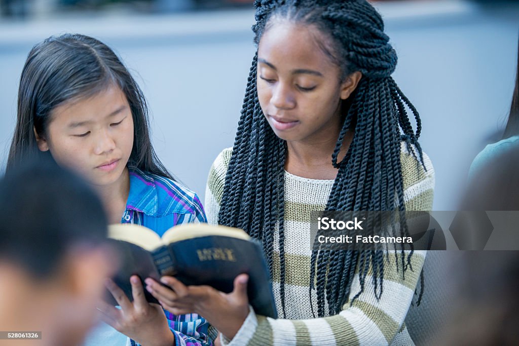 Reading the Bible Together A high school age girl is holding the Bible and is reading it with her fellow classmates during a Bible study. Bible Stock Photo