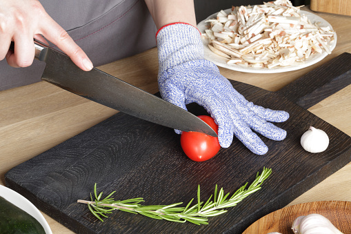 The girl with a knife cuts a tomato on a cutting board