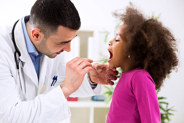 pediatrician examining cute smiling african girl, throat sick - mensentong stockfoto's en -beelden