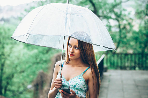 jolie jeune femme avec parapluie sous la pluie à l'aide de téléphone - rain women umbrella parasol photos et images de collection