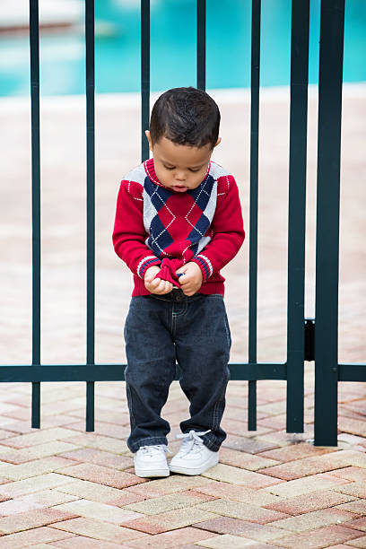 African American toddler boy stands by gate to a pool A young Afro American boy stands by the gate to a pool entrance. Shot with Canon 5D Mark 3. He is trying to look innocent. pool gate stock pictures, royalty-free photos & images
