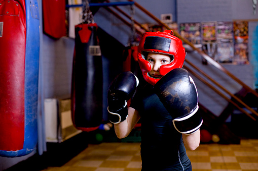 A close up portrait of a young girl aged 11 years, she is wearing protective headgear and boxing gloves ready to compete in a competition.