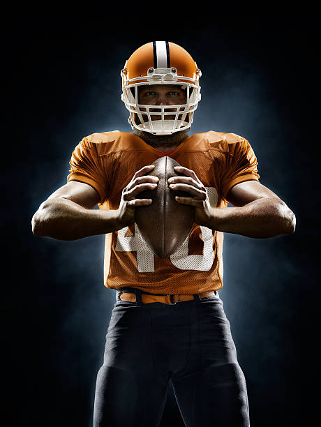 American football player Professional American football player standing on a dark background with spotlight. Player is wearing unbranded football cloths. american football player stock pictures, royalty-free photos & images