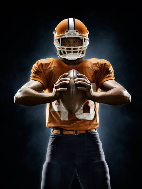 American football player Professional American football player standing on a dark background with spotlight. Player is wearing unbranded football cloths. american football player studio stock pictures, royalty-free photos & images