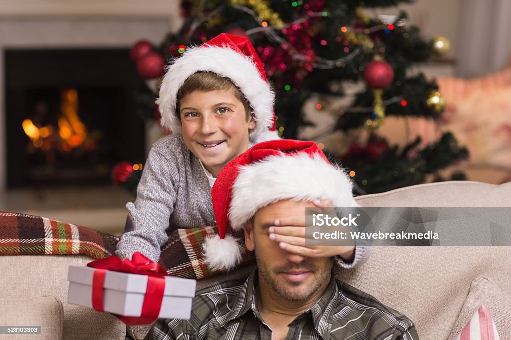 Son surprising his father with christmas gift Son surprising his father with christmas gift at home in the living room 10-11 Years Stock Photo