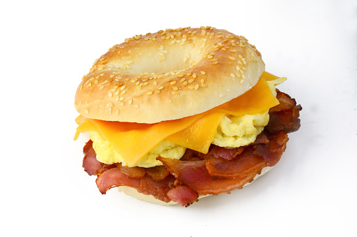 Sesame bagel with scrambled eggs, fried bacon and cheddar cheese. Studio isolated