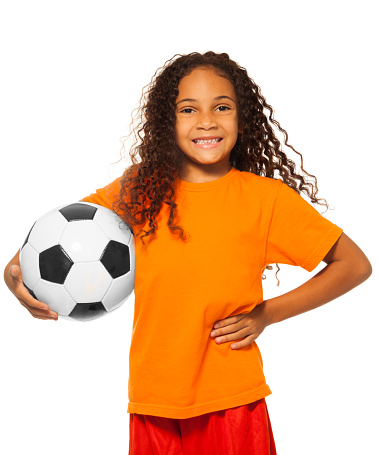Close portrait of happy African black girl with curly hair holding soccer ball and wearing sport team uniform standing isolated on white and smiling 