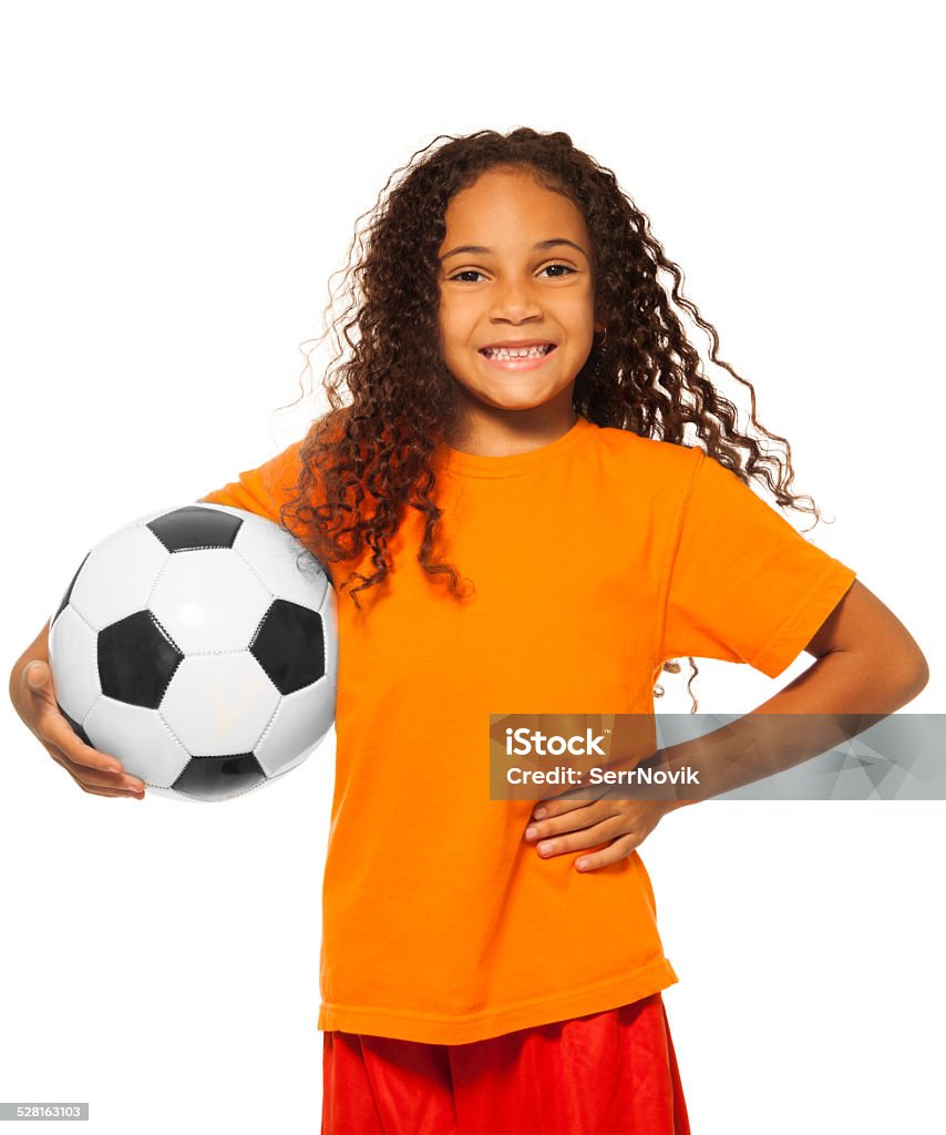 Little African girl holding soccer ball isolated Close portrait of happy African black girl with curly hair holding soccer ball and wearing sport team uniform standing isolated on white and smiling  Girls Stock Photo