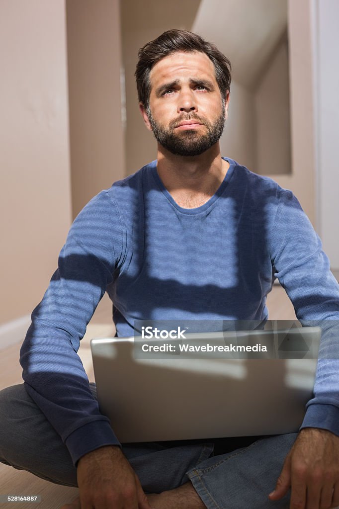 Depressed man sitting on floor using laptop Depressed man sitting on floor using laptop in an empty room  30-39 Years Stock Photo