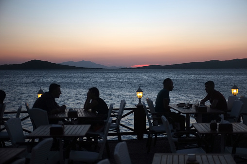 Ayvalik, Turkey - August 29, 2014: People dine in a seaside restaurant at dusk in Ayvalik, Turkey