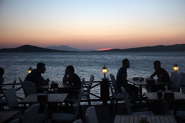 люди, сидя в ресторане на берегу моря на закате - romance lake chair sunset стоковые фото и изображения