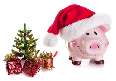 Happy pink piggy bank wearing santa's hat with christmas tree and gifts isolated on a white background