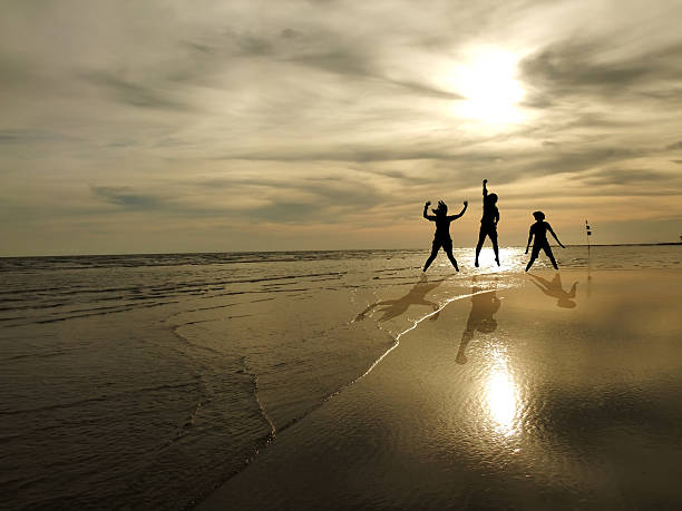 jeunes de sauter sur la plage au coucher du soleil en arrière-plan - spraying beaches summer sunlight photos et images de collection