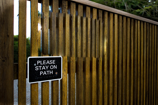A sign on a wooden fence that advises patrons to stay on the path and not wander off.  This could be part of a trail, nature center, or in a national park setting.
