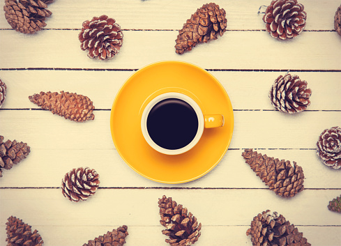 Cup of coffee and pine cone on a white table.