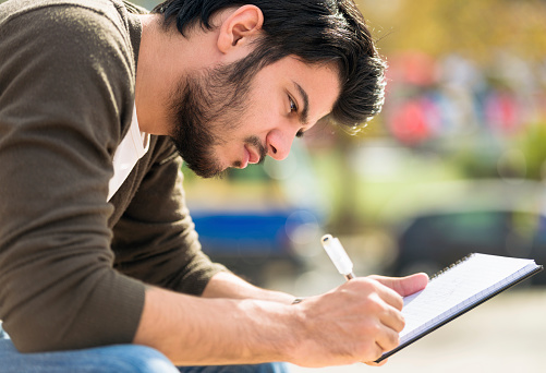 Close-up of a young man writing his journal outdoors.