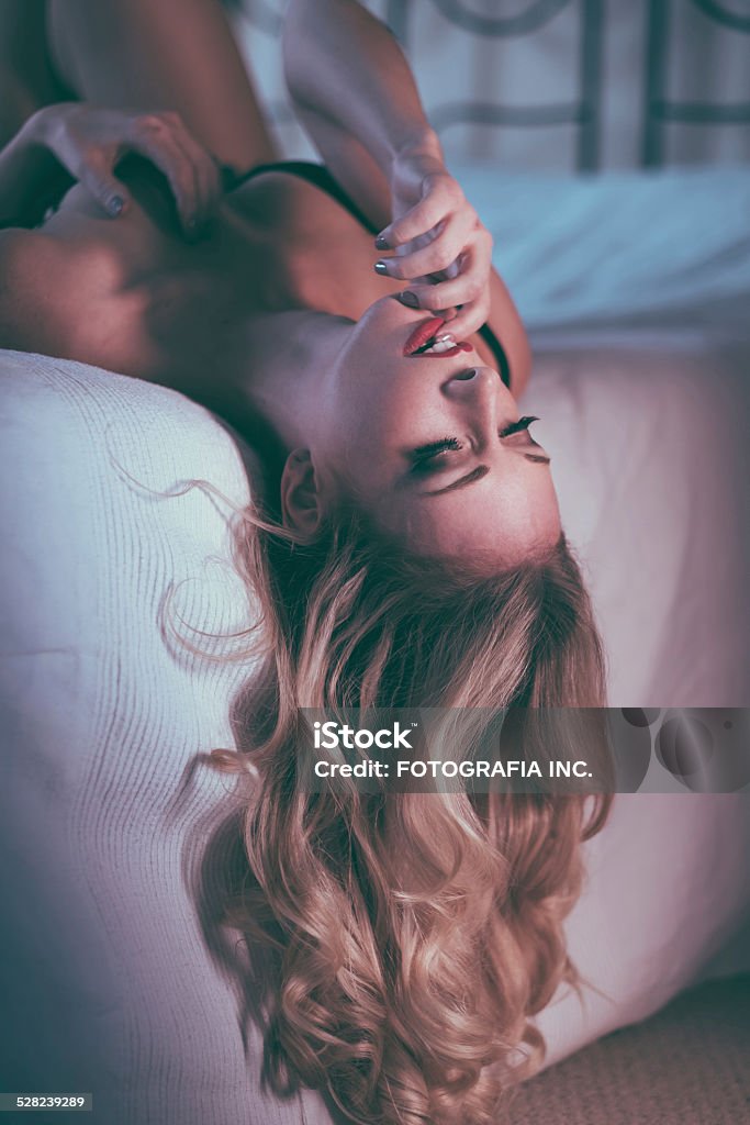 Slim Blonde Young blonde woman posing on her bed. She has slim figure and long wavy hair, wearing lingerie. Head Back Stock Photo