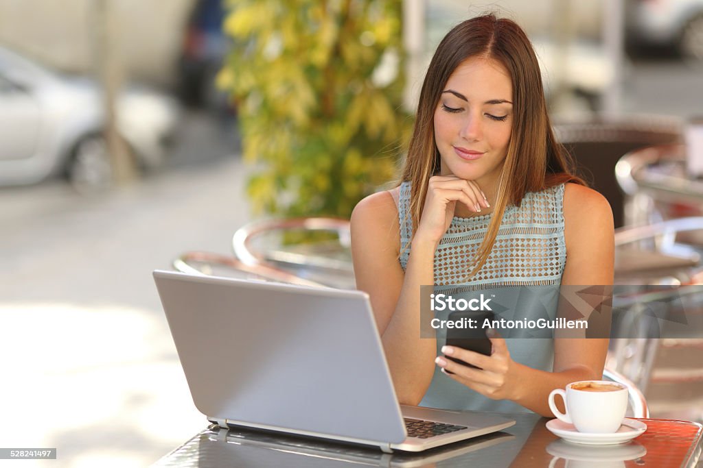 Mujer trabajando con su teléfono y computadora portátil en un restaurante. - Foto de stock de Hotel libre de derechos
