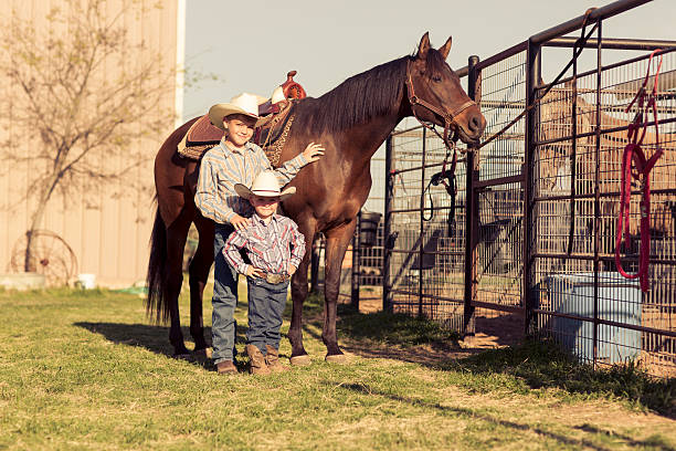 Two young cowboys take a picture with a horse on a ranch in Texas, USA.
