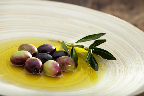 Raw olive and olive oil in wood plate.