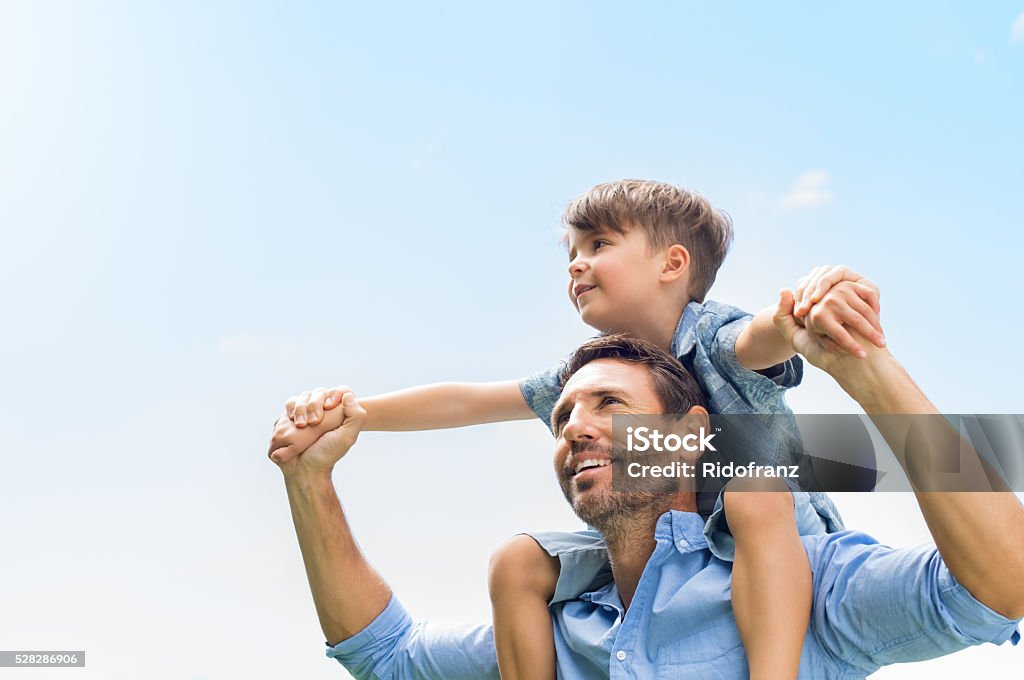 Father and son together Father giving son ride on back in park. Portrait of happy father giving son piggyback ride on his shoulders and looking up. Cute boy with dad playing outdoor. Father Stock Photo