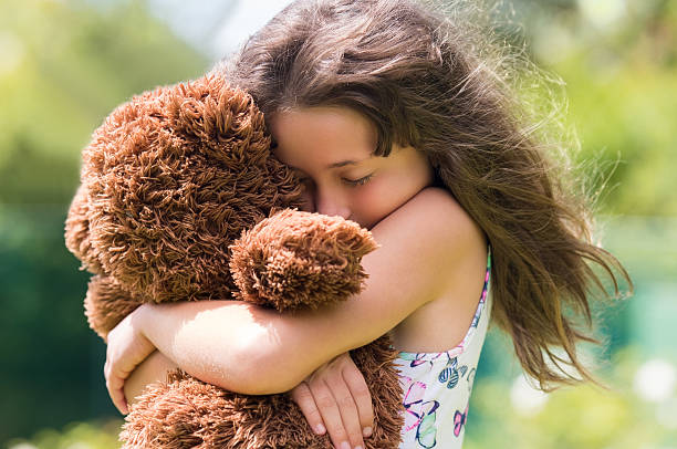 Emotional girl hugging her teddy bear. Young cute girl embracing her brown fur teddy bear. Little girl in love with her stuff toy.