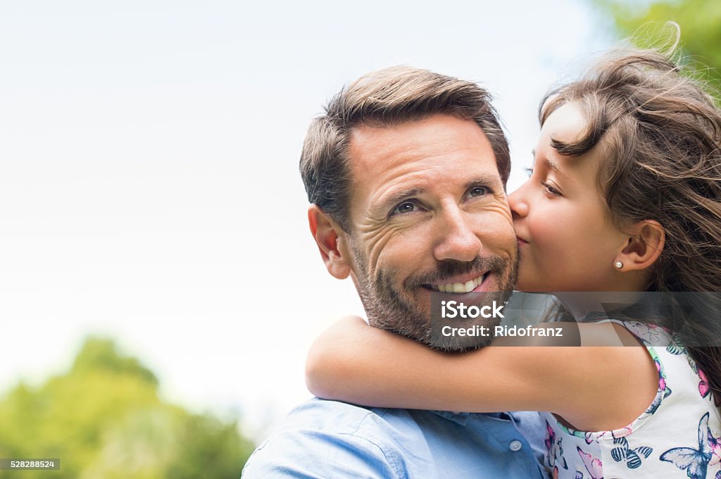 Girl kissing father Portrait of a little girl kissing her dad on cheek. Pretty girl giving a kiss to her father outdoor. Loving child embrace and kissing her father. Father Stock Photo