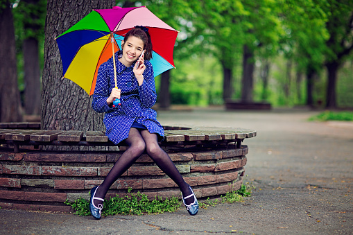 Young teenage girl is talking using her mobile phone in the park in the rainy day.