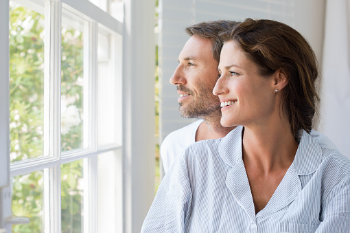 Cheerful young couple looking outside window. Portrait of smiling couple thinking about the future. Happy cheerful couple relaxing at home.
