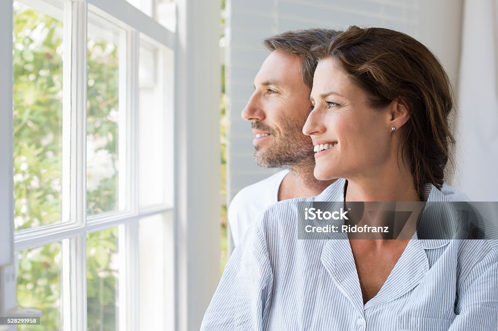 Family future Cheerful young couple looking outside window. Portrait of smiling couple thinking about the future. Happy cheerful couple relaxing at home. Two Parents Stock Photo