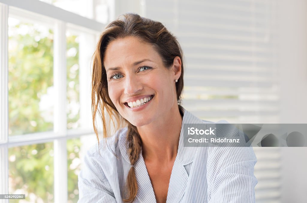 Happy mature woman Portrait of beautiful mature woman sitting and smiling. Woman feeling fresh on a bright sunny morning at home. Woman sitting in nightwear near the window and looking at camera. Women Stock Photo