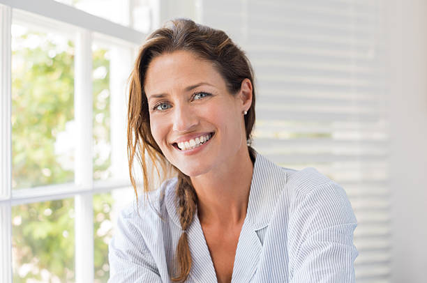 Happy mature woman Portrait of beautiful mature woman sitting and smiling. Woman feeling fresh on a bright sunny morning at home. Woman sitting in nightwear near the window and looking at camera. mid adult women stock pictures, royalty-free photos & images