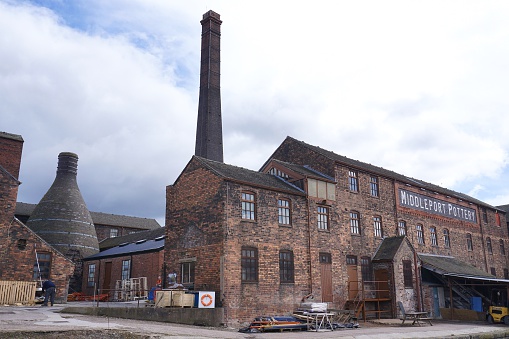 Stoke-on-Trent, UK - March 29, 2016: Two men work in yard of the historic, still-active Middleport Pottery factory in Burslem, Stoke-on-Trent, as seen from the adjacent public canal path.