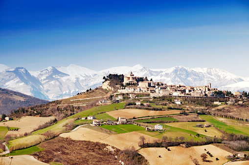 Panorama over a beautiful rural and rolling landscape and a village upon the hill in the Marche region of Italy. The snow capped mountains Sibillini in the background. Picture was taken in springtime.