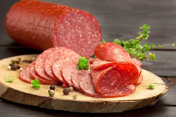 halved in slices turkey salami served on a slice of wood with thyme and ground pepper