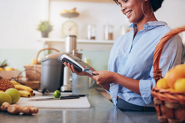 Juice bar credit card payment. Female employee in a juice bar swiping a credit card in a card reader machine. African woman standing at checkout counter. smart card stock pictures, royalty-free photos & images