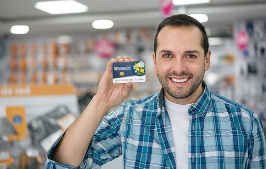 Man at a tech store holding a rewards card to enjoy special benefits. Design on card is own design.