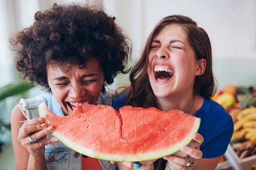 Close up portrait of two young girls enjoying a watermelon. Female friends eating a watermelon slice and laughing together.