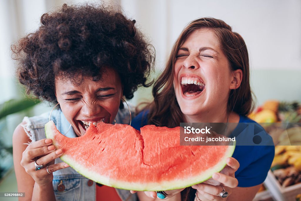Two young girls enjoying a watermelon Close up portrait of two young girls enjoying a watermelon. Female friends eating a watermelon slice and laughing together. Eating Stock Photo