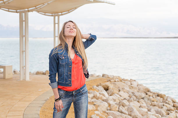 Beautiful young blond woman standing sea beach, posing, wearing jeans, Dead sea Israel.