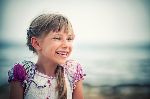 Portrait of a little girl laughing. Sea visible in the background. The girl aged 6 is wearing a dress. Closeup portrait. 