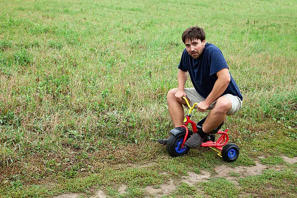 Adult man tying to ride on a small tricycle